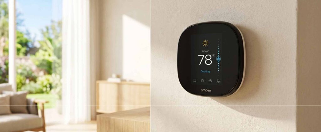 A smart thermostat is mounted on a light-colored wall in a bright, modern living room. The display shows an indoor temperature of 78 degrees—often considered the best AC setting for summer—while cooling mode is active and sunlight streams through large windows.