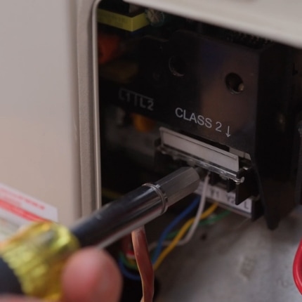 A close-up of a person's hand using a screwdriver to adjust or repair wiring inside an electronic device, with visible wires and a panel labeled "CLASS 2.