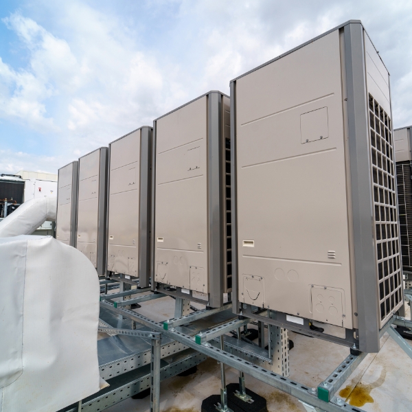 Outdoor commercial HVAC units are installed in a row on a rooftop platform with a metal support structure, set against a cloudy sky.